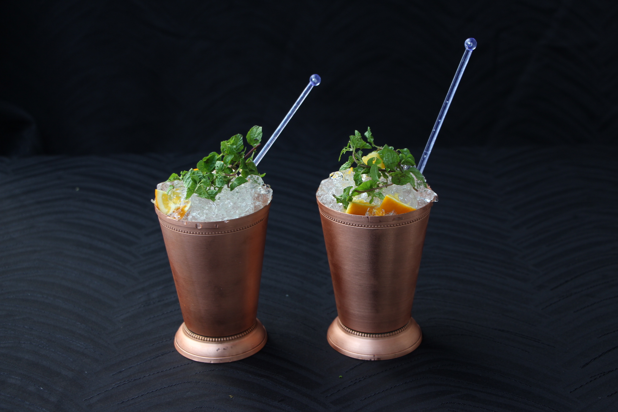 Two cocktails with straws against dark backdrop